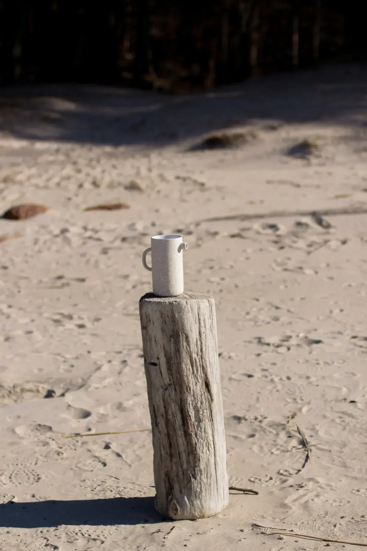 Handmade ceramic mug on weathered wooden post by the sea